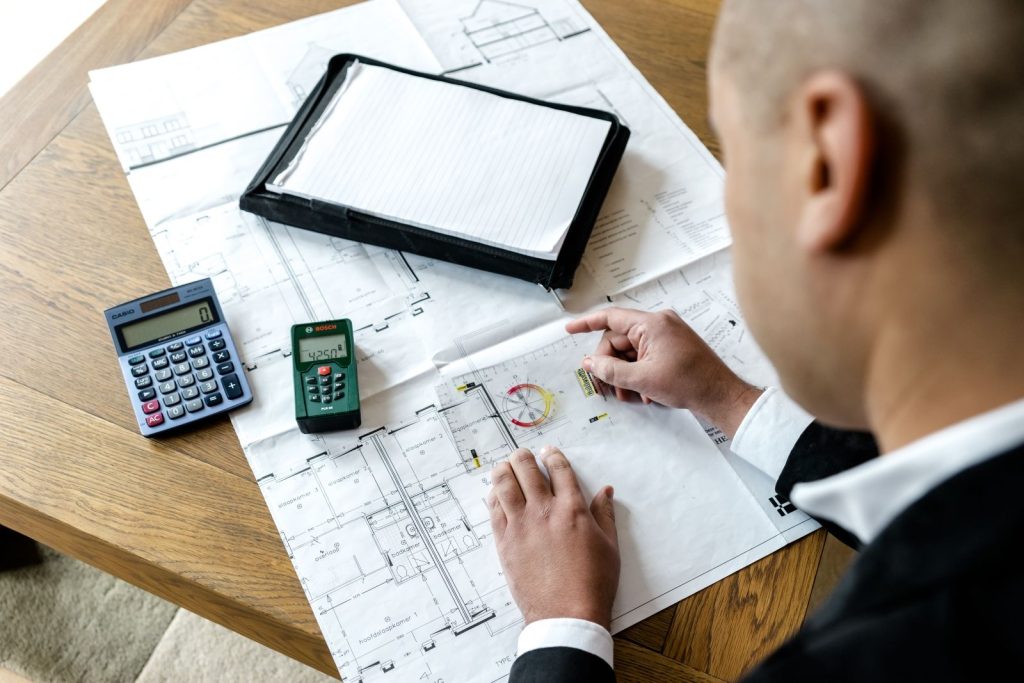Architect bekijkt bouwtekeningen met rekenmachine en meetapparaat.