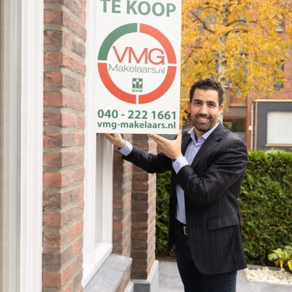 Makelaar plaatst te koop bord bij bakstenen huis.