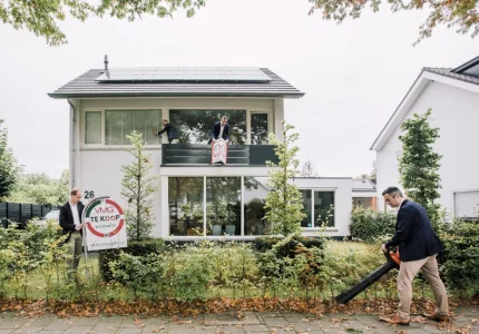 Huis te koop met mensen en bladblazer in tuin.