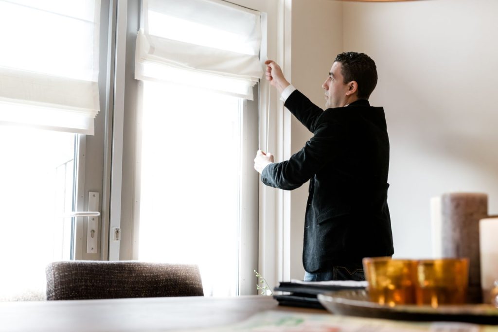 Man opent gordijnen bij raam in woonkamer.
