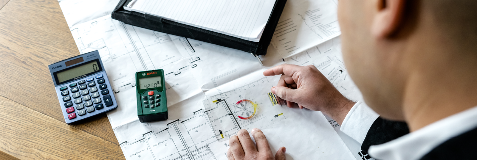 Man bestudeert bouwtekeningen met rekenmachines en notitieboek